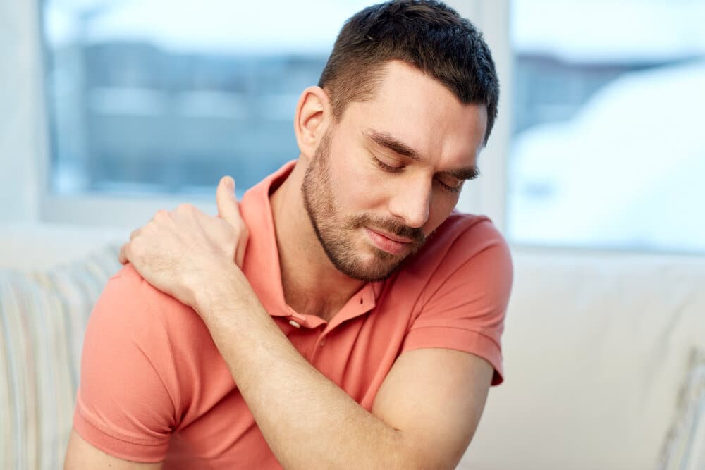 people, healthcare and problem concept - unhappy man suffering from neck or shoulder pain at home